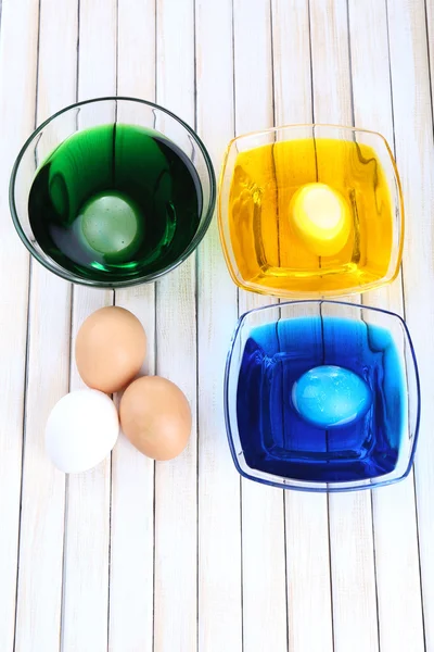 Чаши с краской для пасхальных яиц и яиц на деревянном столе — стоковое фото