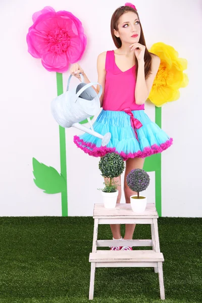Krásná mladá žena v drobné sukni, zalévání květin na dekorativní pozadí — Stock fotografie