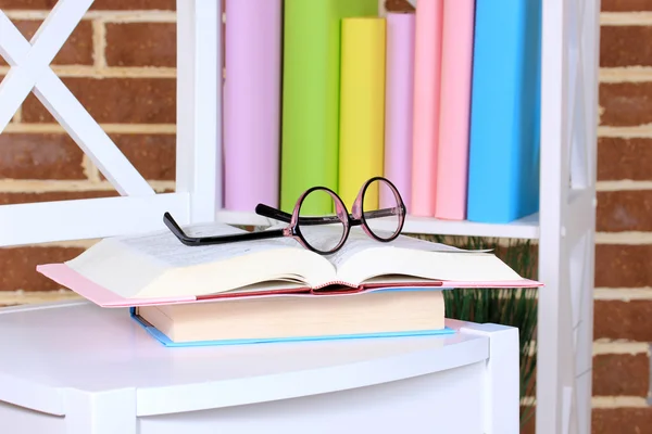 Samenstelling met glazen en boeken, op stoel, op kabinet en muur achtergrond — Stockfoto