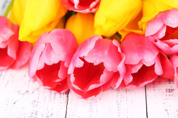 Růžové a žluté tulipány na dřevěný stůl — Stock fotografie
