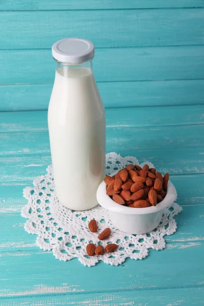 Amandelmelk in fles met amandelen in kom, op een houten achtergrond kleur — Stockfoto