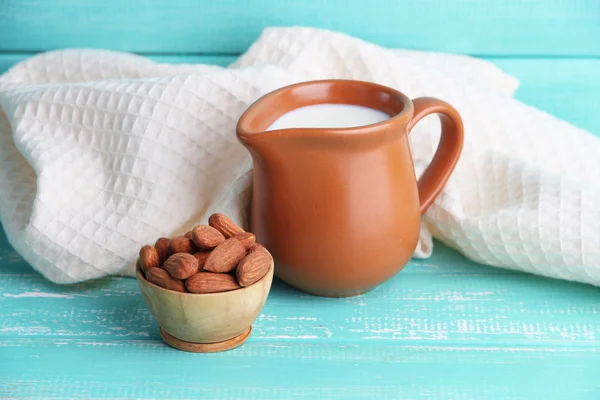 Almond milk in jug with almonds in bowl, on color wooden background — Stock Photo, Image