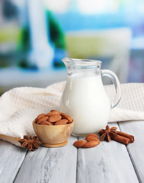 Latte di mandorla in brocca con mandorle in ciotola, su tavolo di legno a colori, su sfondo brillante — Foto Stock