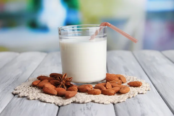 Susu almond dalam gelas dengan almond, di atas meja kayu berwarna, di latar belakang cerah — Stok Foto