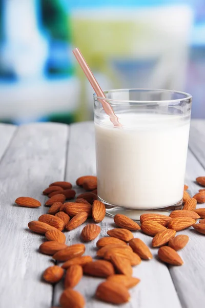 Leche de almendras en vaso con almendras, sobre mesa de madera de color, sobre fondo brillante —  Fotos de Stock