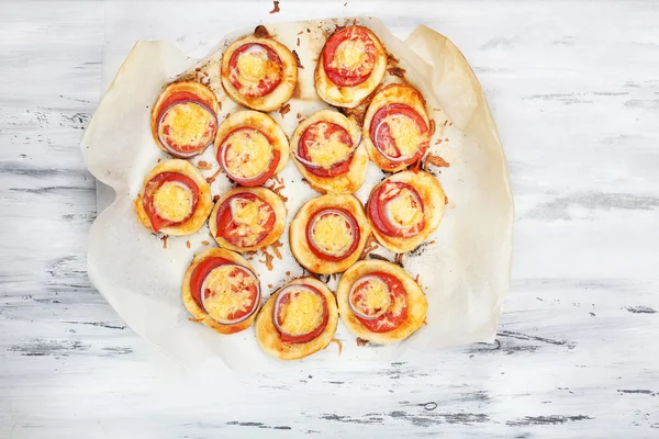Small pizzas on baking paper on wooden table — Stock Photo, Image