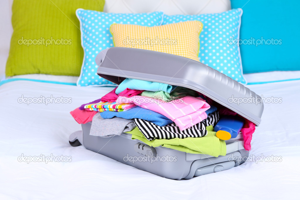 Grey suitcase with clothing on bed close-up