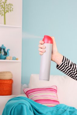 Sprayed air freshener in hand on home interior background clipart