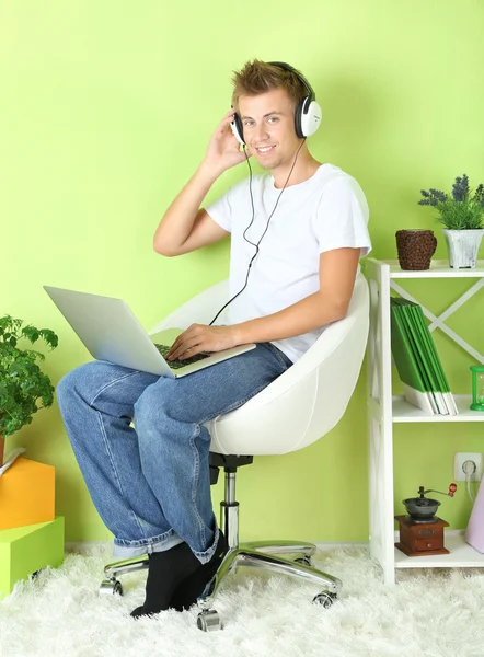 Jovem relaxante com laptop em poltrona, em casa fundo interior — Fotografia de Stock