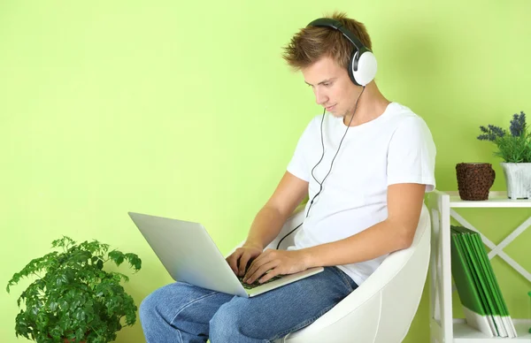 Ung man avkopplande med laptop i fåtölj, på hem inredning bakgrund — Stockfoto