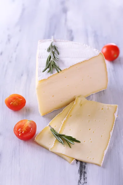 Tasty Camembert cheese with tomato and rosemary, on wooden table — Stock Photo, Image