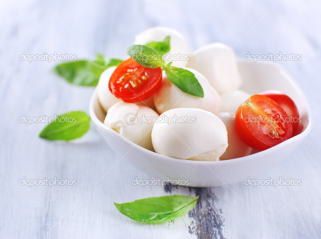 Tasty mozzarella cheese with basil and tomatoes in bowl, on wooden table