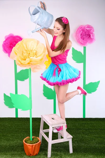 Hermosa mujer joven en falda pequeña regar flor sobre fondo decorativo — Foto de Stock