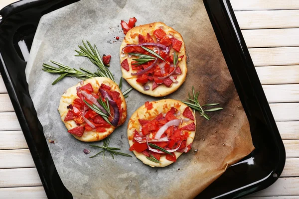 Pequeñas pizzas sobre papel de hornear de cerca —  Fotos de Stock