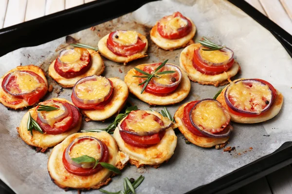 Pequeñas pizzas sobre papel de hornear de cerca — Foto de Stock