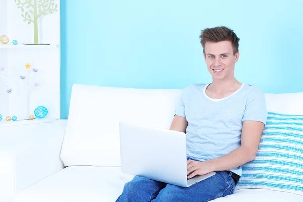Cara sentado no sofá com laptop no fundo azul — Fotografia de Stock