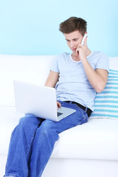 Kerel praten van telefoon met laptop op blauwe achtergrond — Stockfoto