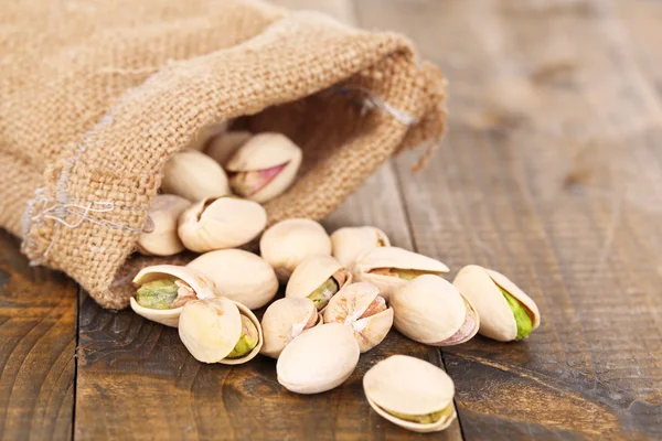Pistachio nuts in sackcloth bag on wooden background — Stock Photo, Image