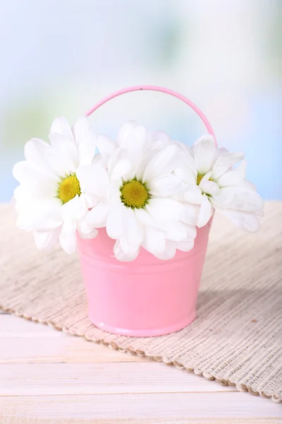 Vackra chrysanthemum blommor i hinken på bordet på ljus bakgrund — Stockfoto