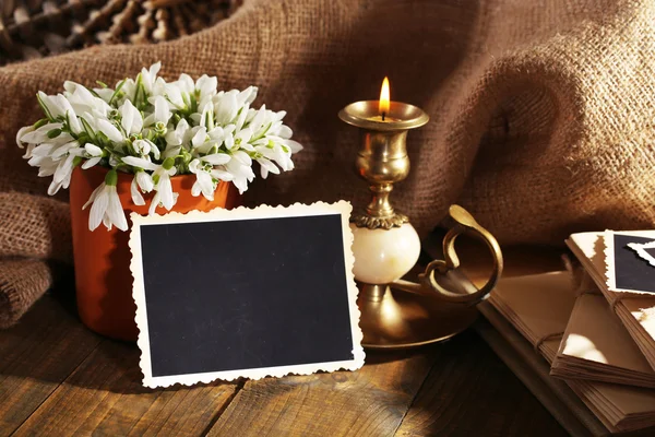 Composition with beautiful snowdrops in vase, candle, old letters and photos on wooden table on sackcloth background — Stock Photo, Image