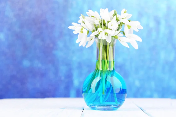 Krásný sněženky v váza, na dřevěný stůl na světlé pozadí — Stock fotografie