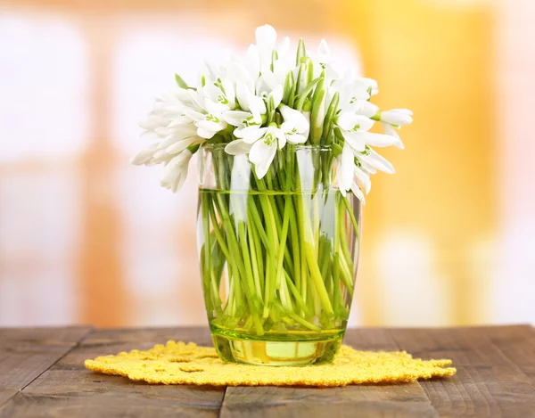 Beautiful snowdrops in vase, on wooden table on bright background — Stock Photo, Image