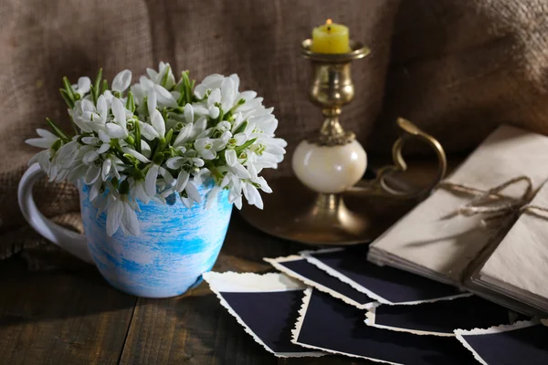 Sammansättning med vackra snödroppar i vas, ljus, gamla brev och foton på träbord på säckväv bakgrund — Stockfoto