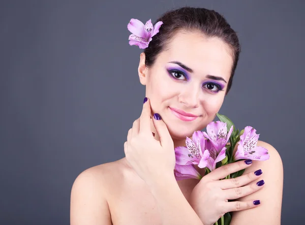 Vacker ung kvinna med blommor på grå bakgrund — Stockfoto
