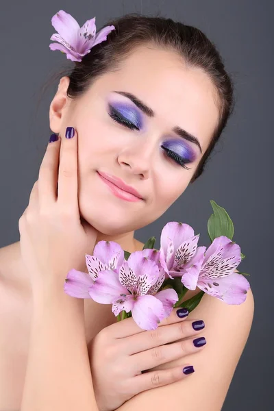 Schöne junge Frau mit Blumen auf grauem Hintergrund — Stockfoto