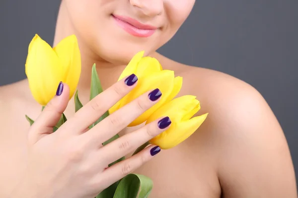 Mladá žena s květinami na šedém pozadí — Stockfoto