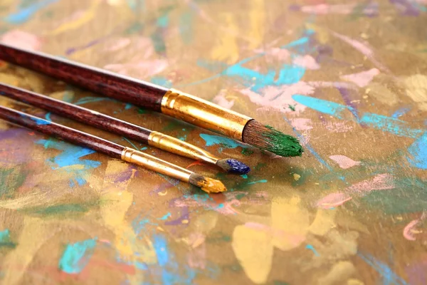 Muitas escovas em tintas em fundo de madeira multicolor — Fotografia de Stock