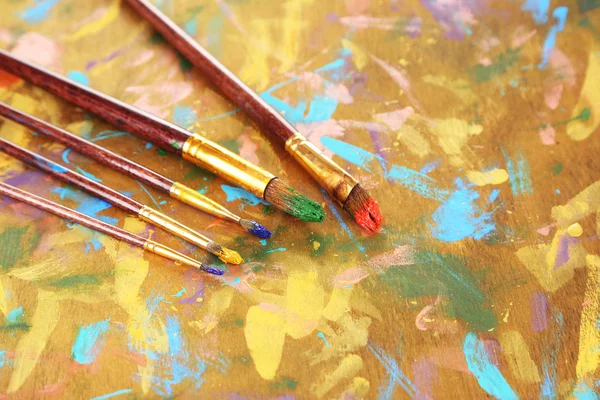 Muitas escovas em tintas em fundo de madeira multicolor — Fotografia de Stock