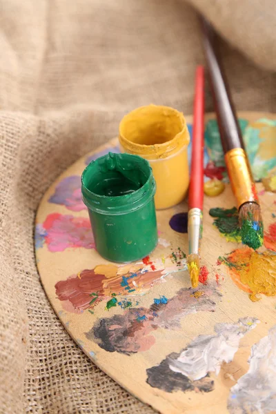 Composition with brushes on used wooden palette, on sackcloth background — Stock Photo, Image