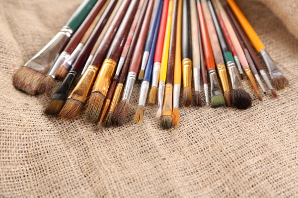 Many brushes in paints on sackcloth background — Stock Photo, Image