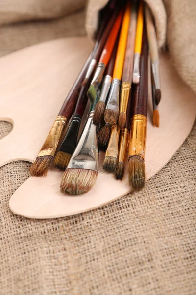 Many brushes in paints on sackcloth background — Stock Photo, Image