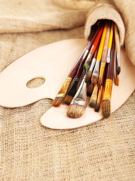 Many brushes in paints on sackcloth background — Stock Photo, Image