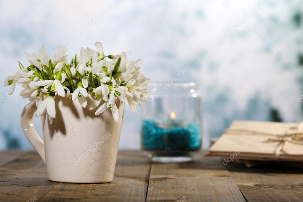 Composition with beautiful snowdrops in vase, candle, old letters and photos on wooden table on bright background