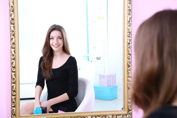 Joven hermosa mujer sentada frente al espejo en la habitación — Foto de Stock