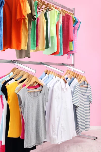 Διαφορετικά ρούχα σε κρεμάστρες, σε ροζ φόντο — Φωτογραφία Αρχείου