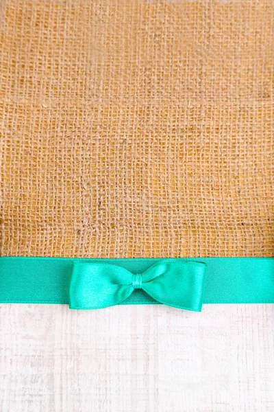 Sackcloth with color ribbon and bow on wooden background — Stock Photo, Image