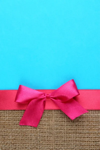 Sackcloth with color ribbon and bow on color paper background — Stock Photo, Image