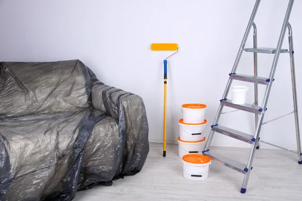 Baldes com tinta, sofá embrulhado e escada no fundo da parede. Foto conceitual de obras de reparação no quarto — Fotografia de Stock