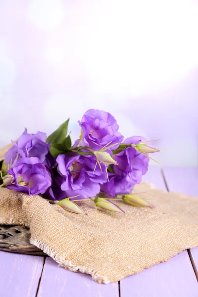 Фиолетовая искусственная эустома на мешковине на цветном деревянном столе, на ярком фоне — стоковое фото