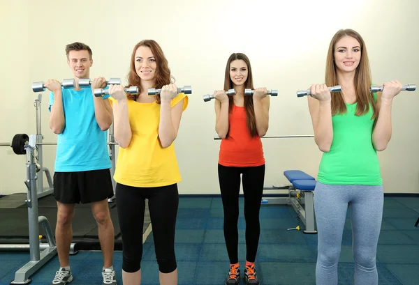 Jeunes belles personnes engagées avec des haltères dans la salle de gym — Photo