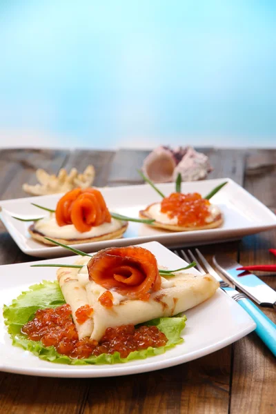 Pannenkoeken met rode kaviaar, zalm en mayo, groene ui, op plaat, op houten tafel, op lichte achtergrond — Stockfoto