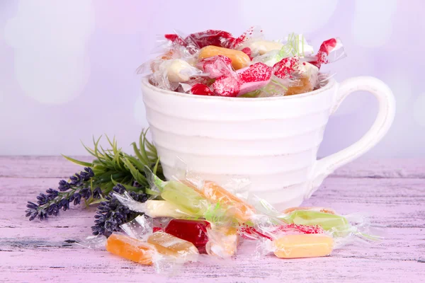 Tasty candies in mug with flowers on table on bright background — Stock Photo, Image