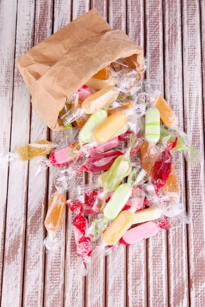 Sabrosos caramelos en bolsa de papel sobre fondo de madera — Foto de Stock