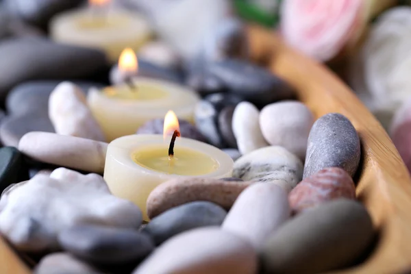 Bol en bois avec pierres de spa et bougies sur table en bois, sur fond de fleurs — Photo