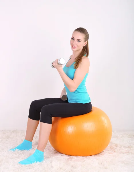 Young beautiful fitness girl exercising with orange ball and dumbbells in gym — Stock Photo, Image