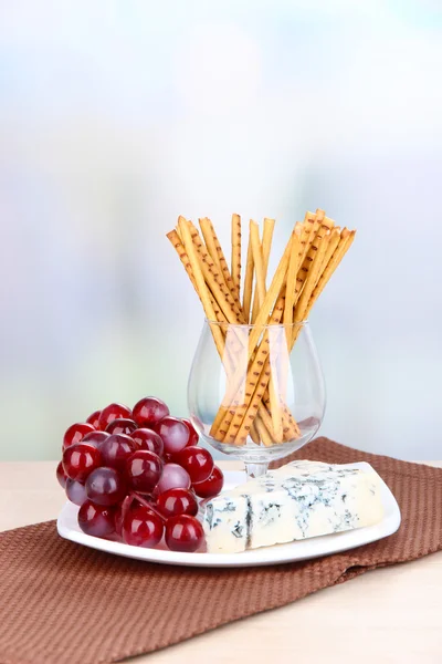 Cheese, grape and bread sticks on plate on wooden table, on light background — Stock Photo, Image